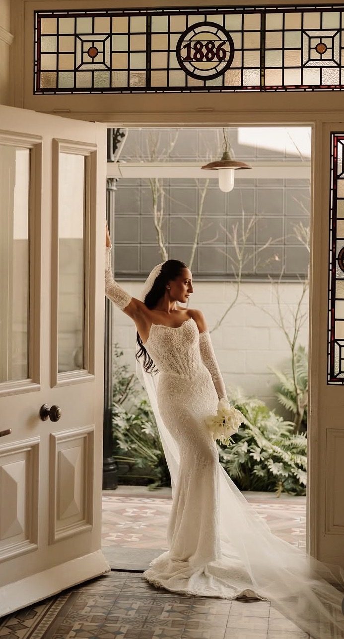 Rayya in her wedding gown and cathedral veil, standing in a heritage doorway